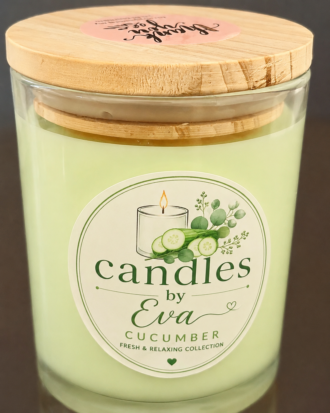 A glass jar candle with pale green wax and a light wood lid, labeled 'candles by Eva Cucumber Fresh & Relaxing Collection'.